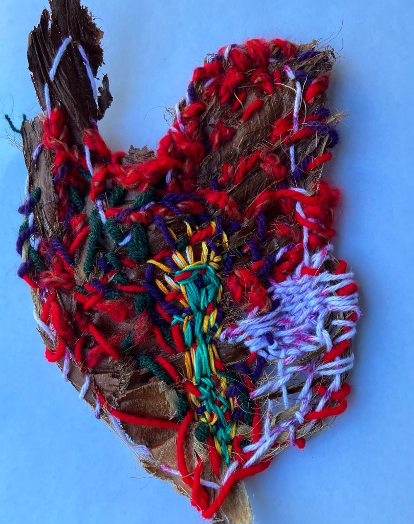A hand stitched heart of various fibers on palm fiber.