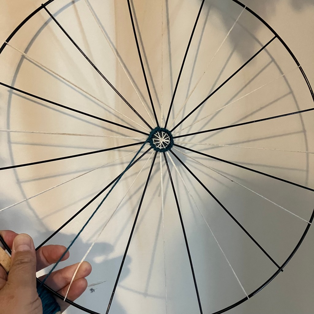 The start of the current project by fiber artist, Sarah Batchelder - a metal wreath frame with warp strings added and a tiny green ring in the center.