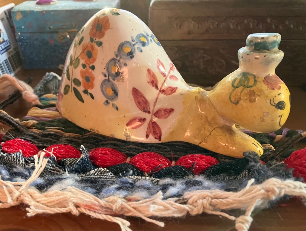 A colorful ceramic snail on top of a handmade weaving by Sarah Batchelder.