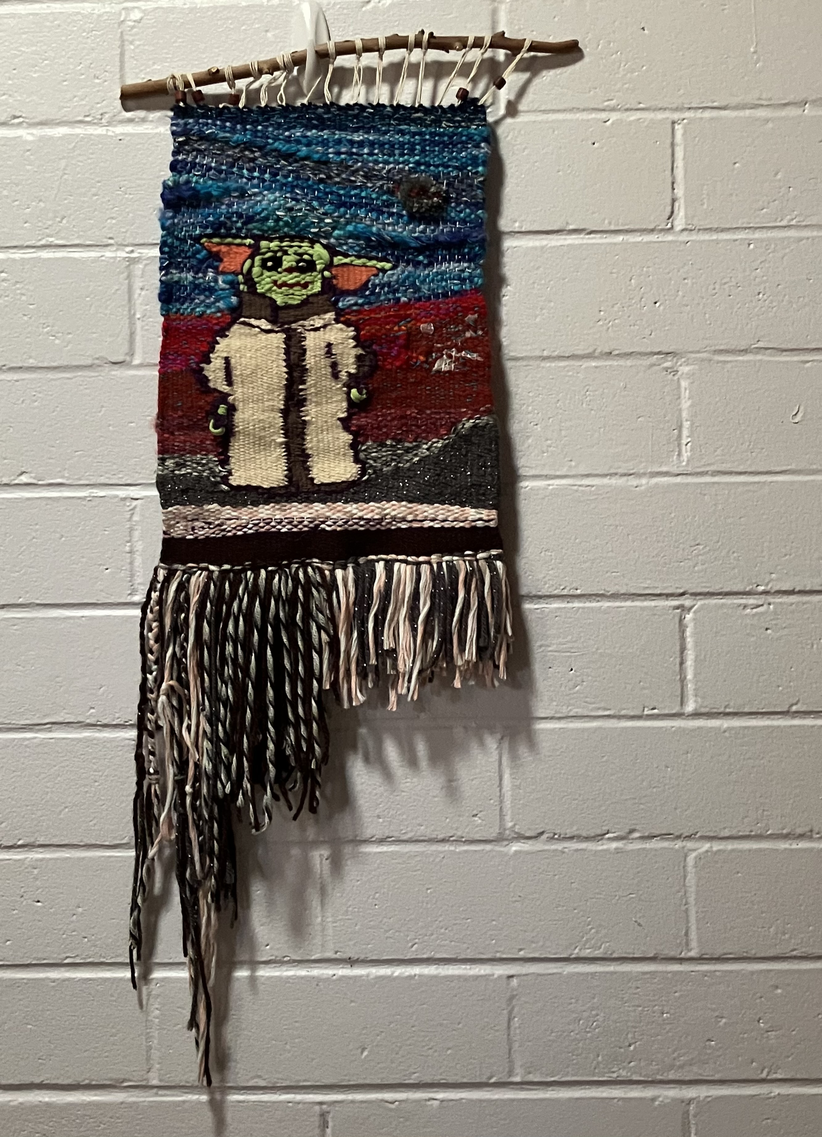 A handwoven image depicting Grogu aka Baby Yoda smiling on an alien landscape.