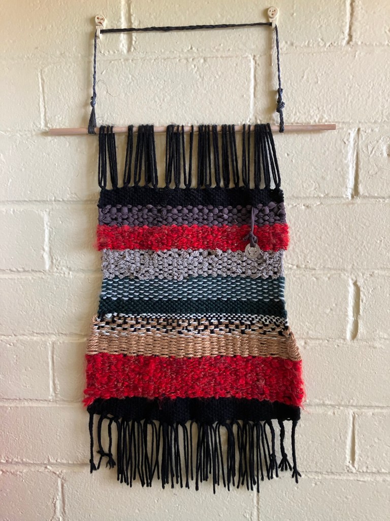 Handmade wall hanging / handwoven tapestry by fiber artist Sarah Batchelder. The tapestry is made from various yarns, jute twine, and repurposed fabrics. It also includes an old NYC subway token.