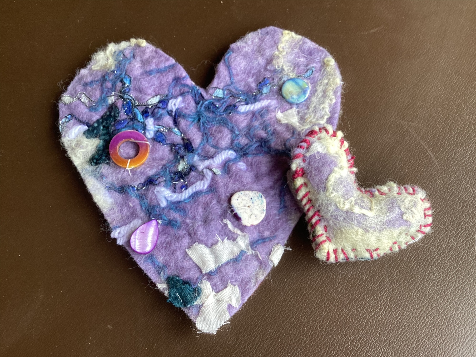 Two hand felted hearts. One is a heart shaped bead and the other has beads on it.
